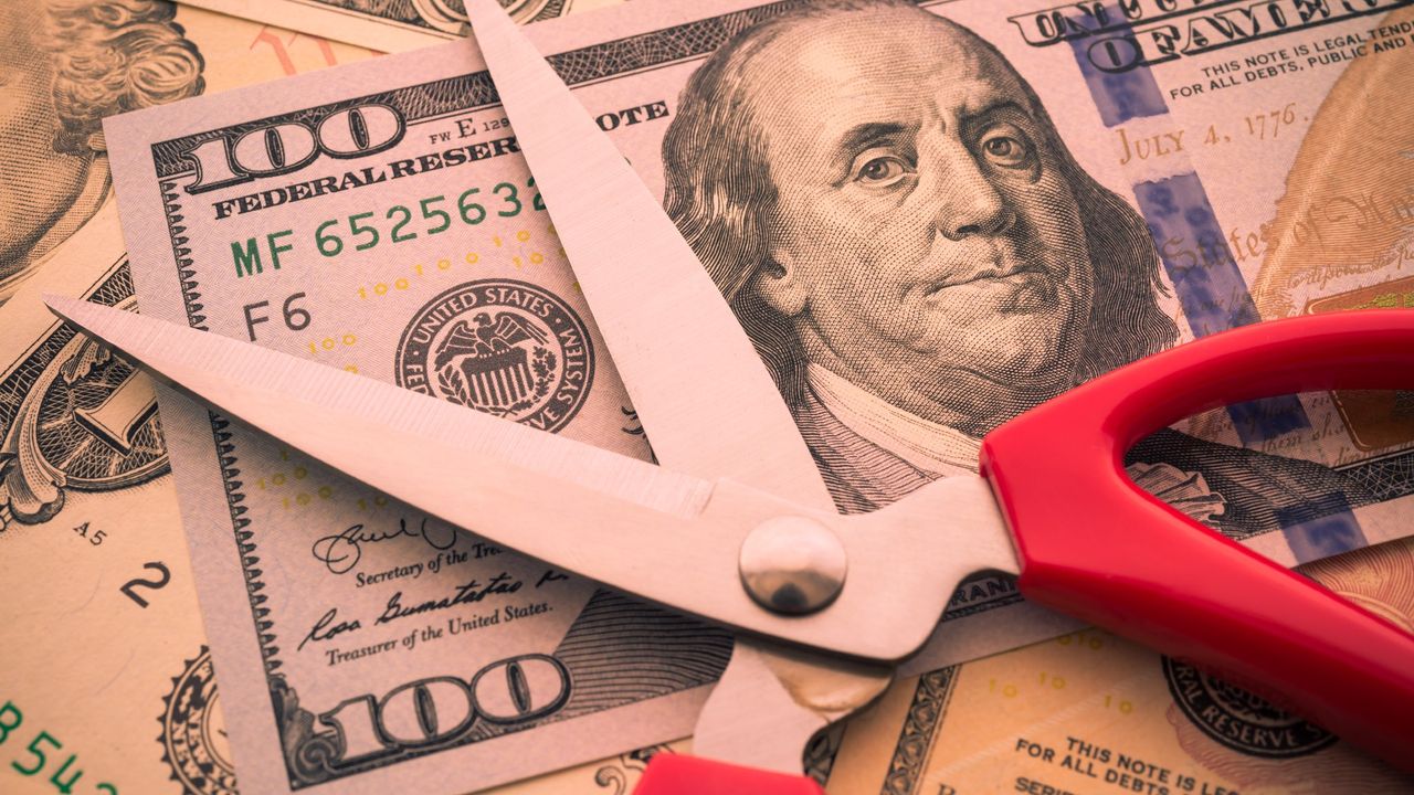 Pair of red scissors sitting on top of 100 dollar bill