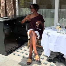 Woman sitting in chair wearing brown top, white shorts and sandals