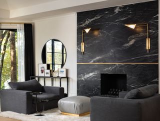 black and cream living room with black marble wall and black low slung armchairs, grey footstool, gold wall lights, black console and mirror