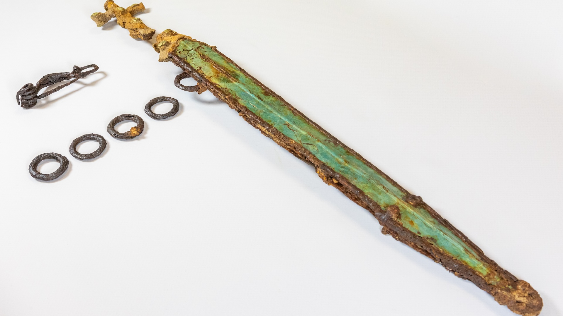 a weathered decorated sword next to metal belt rings and a brooch