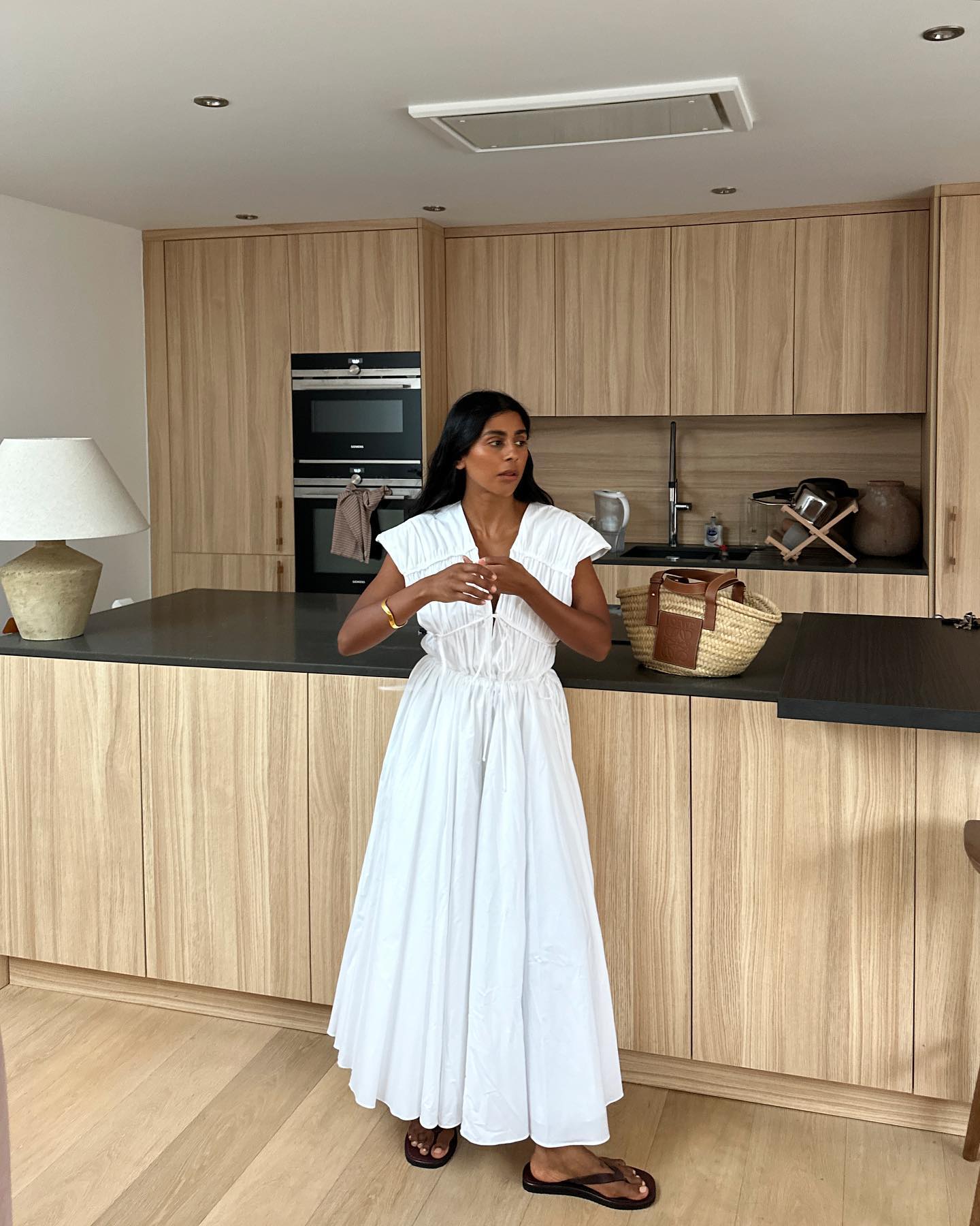woman wears white summer dress with black flip flops and woven basket bag