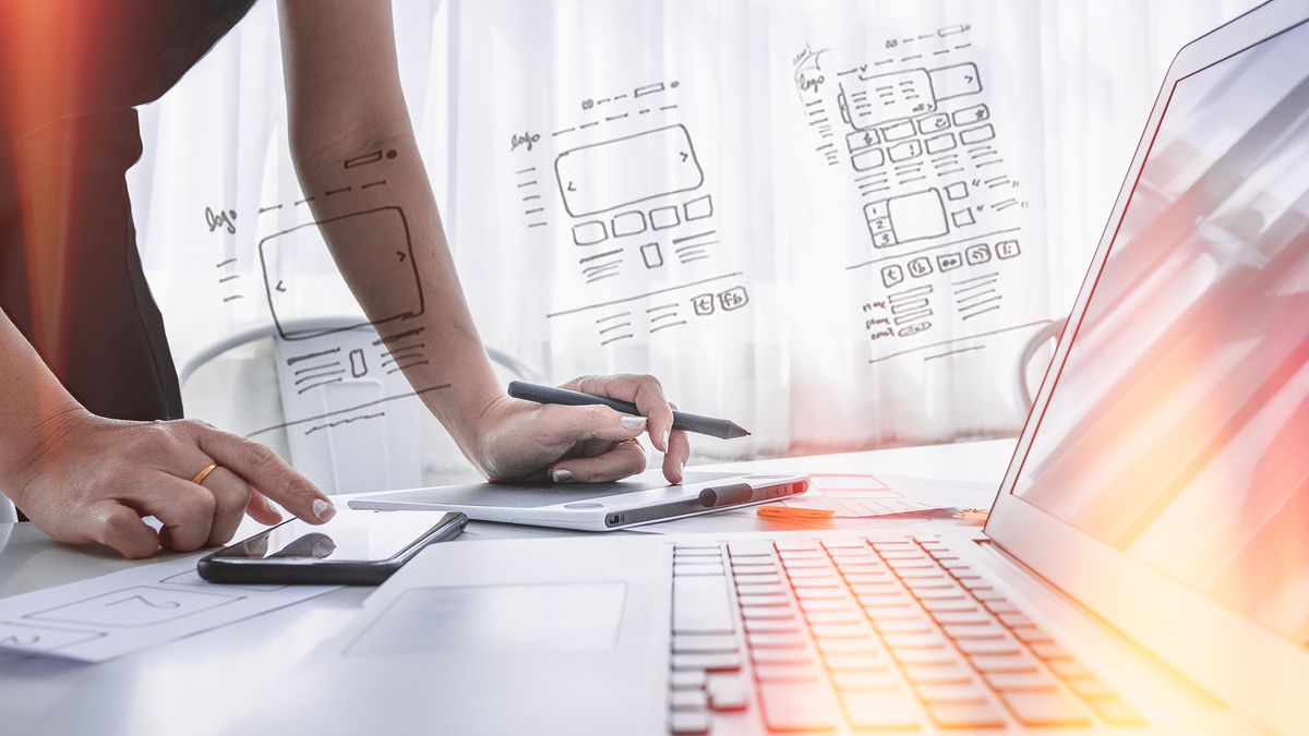 A UX designer using a laptop and a smartphone while planning new webpage layouts