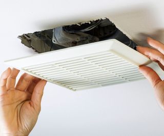 Close up horizontal photo of female hands removing bathroom fan vent cover from ceiling