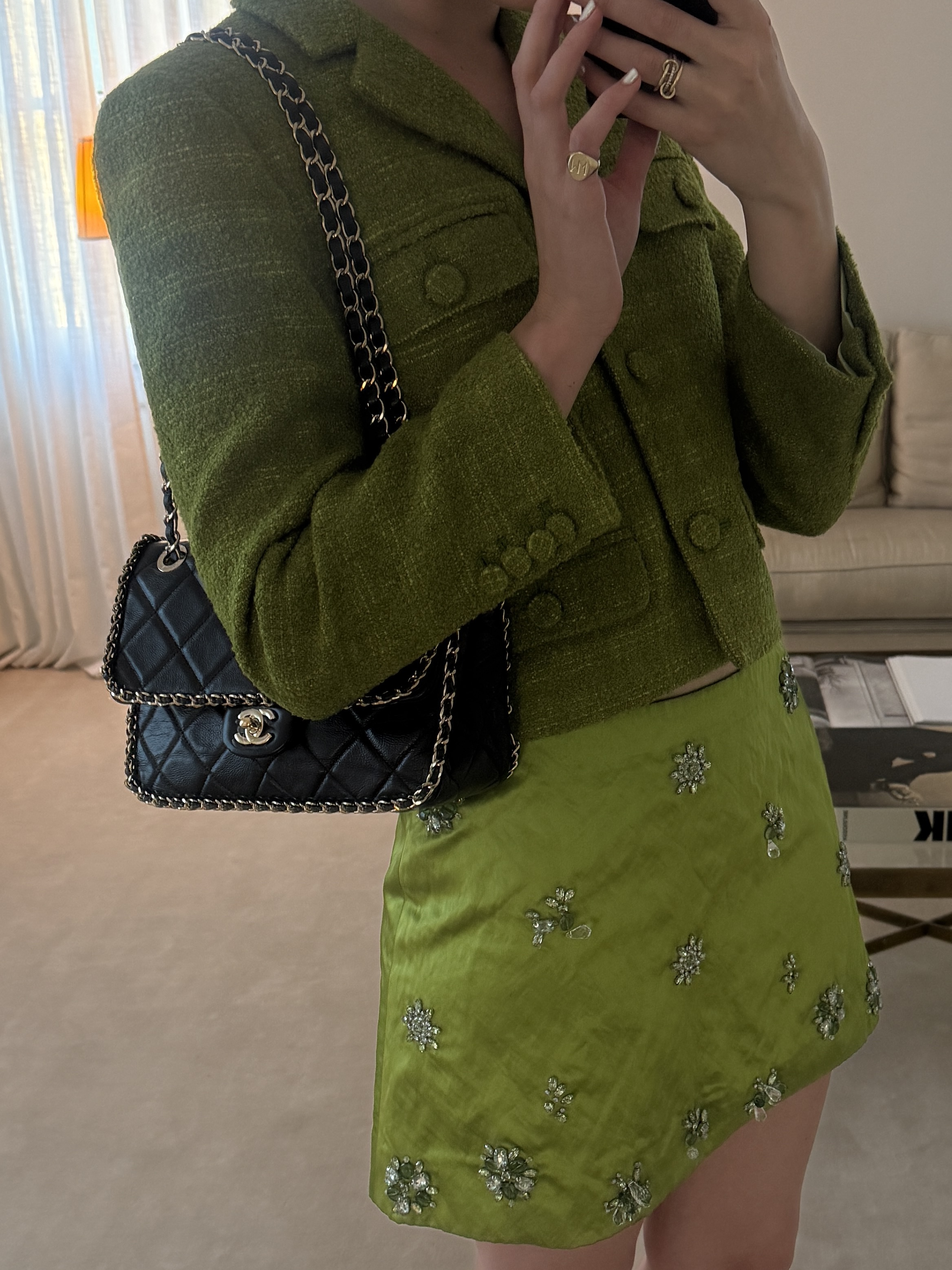 Christie Tyler wears a green cropped tweed jacket over a silk, bead-embellished green mini skirt with a chain-lined Chanel flap bag