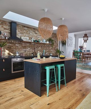 An open-plan kitchen with black wooden kitchen island, wooden flooring and exposed brick wall