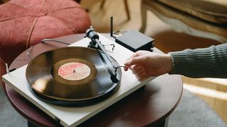 Pro-Ject Primary E1 turntable with a hand putting the needle on a vinyl