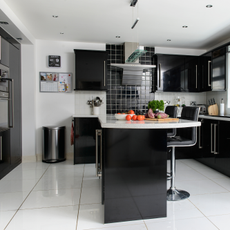Modern kitchen with black, glossy cupbard, silver metal bin and white flooring.