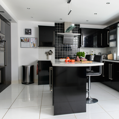 Modern kitchen with black, glossy cupbard, silver metal bin and white flooring.