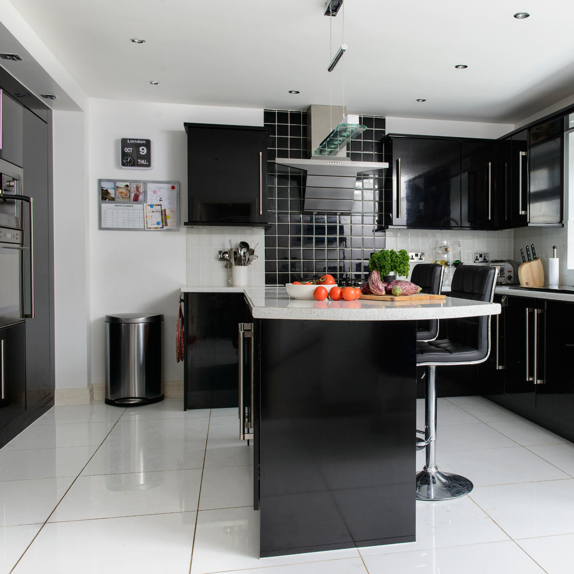 Modern kitchen with black, glossy cupbard, silver metal bin and white flooring.