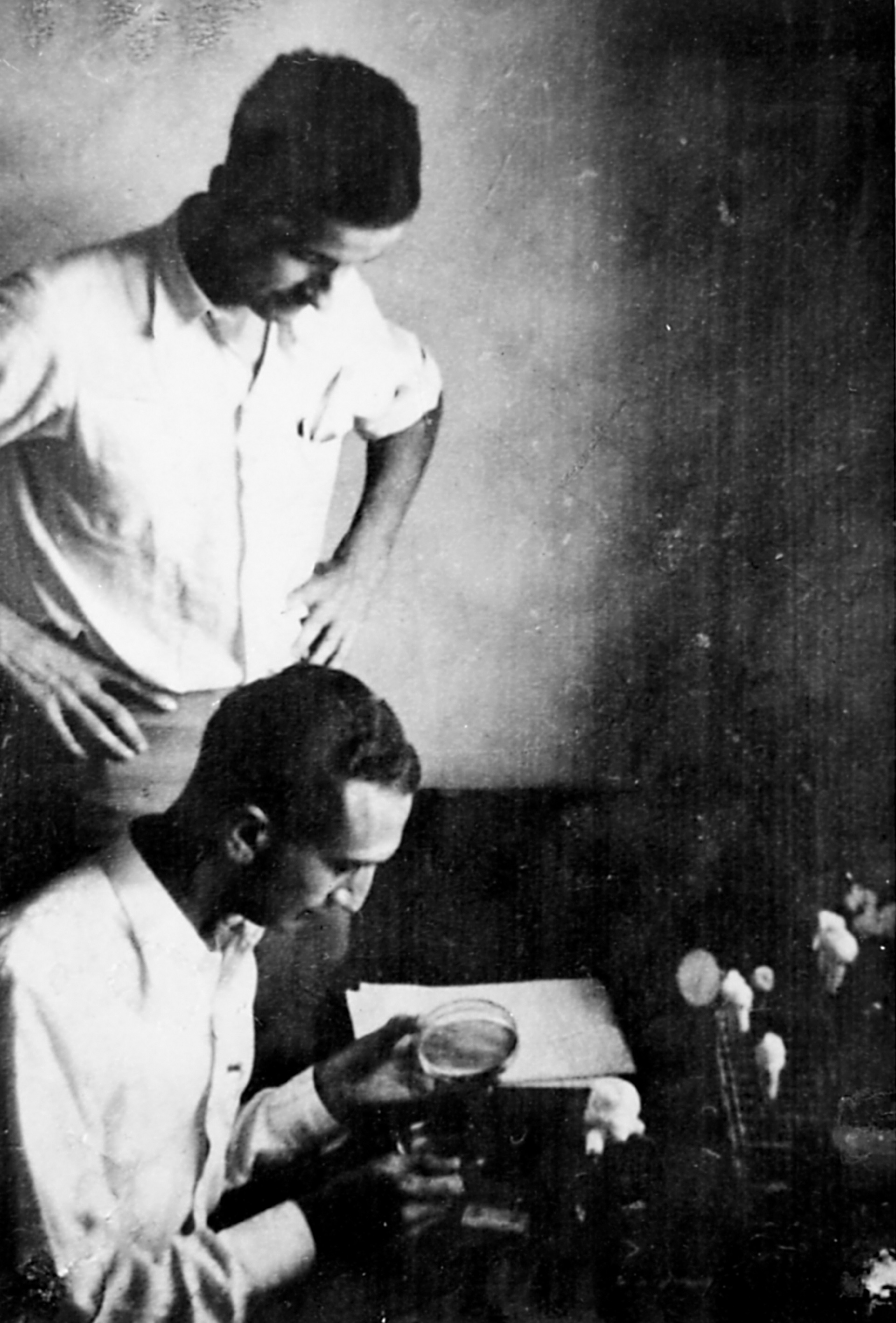 a black and white image of Max Delbruck and Salvador Luria looking at a petri dish in a laboratory