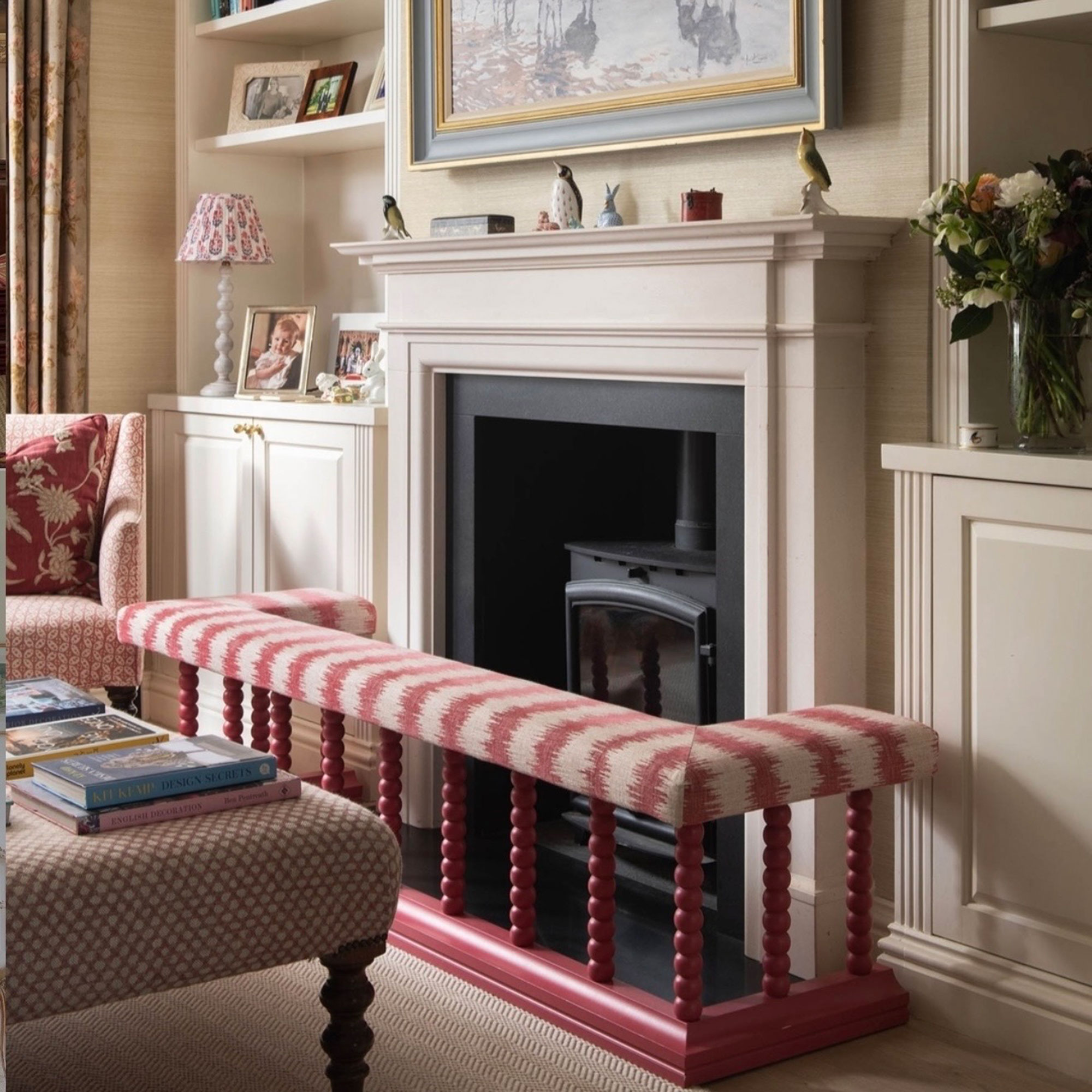 Neutral living room with fireplace, built in storage and red and white striped upholstered fireplace fender surround