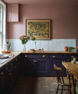 Pink painted kitchen with blue cabinetry, wooden countertop, wooden dining table, artwork on wall