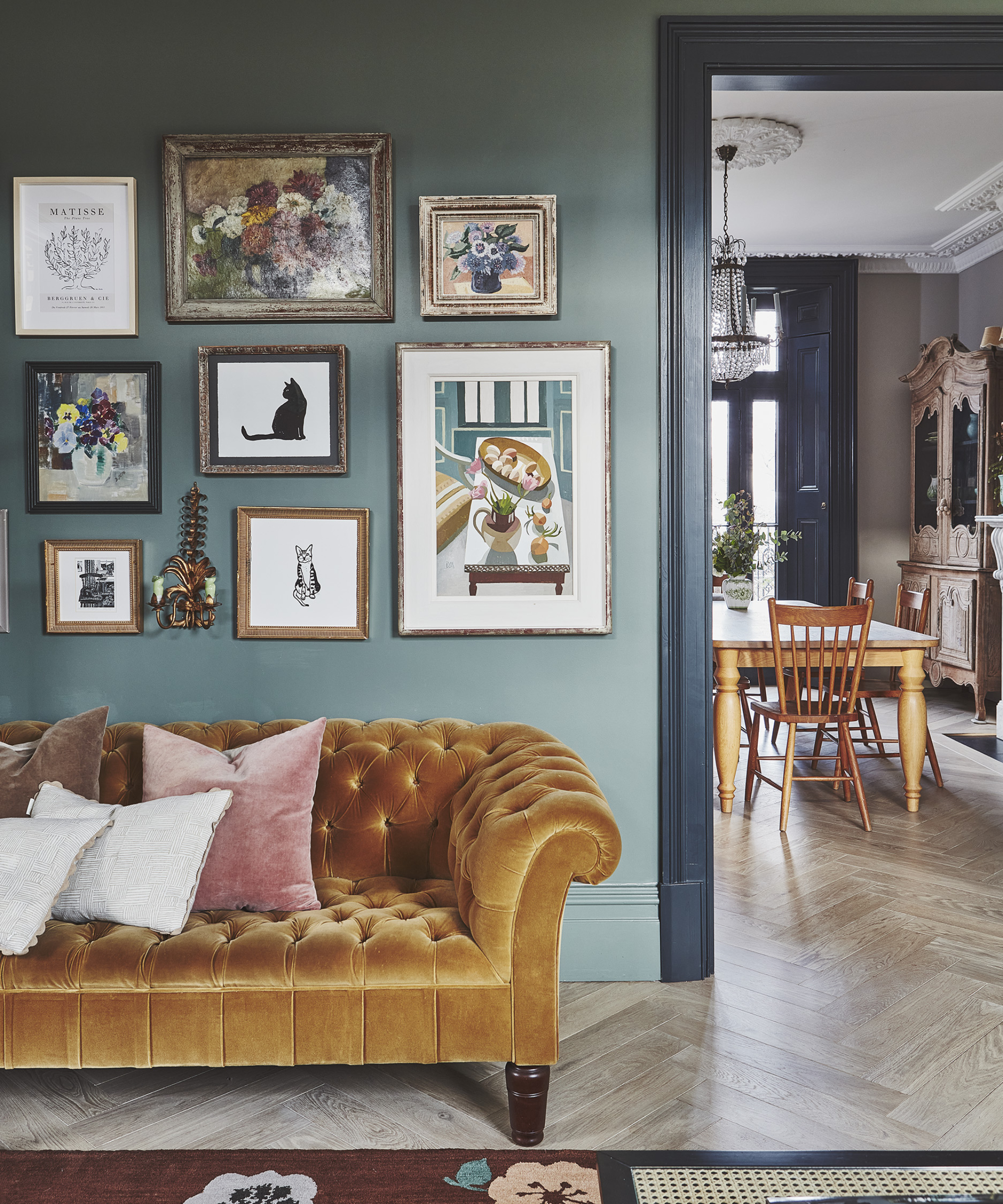 living room leading to dining room with blue walls and darker blue woodwork, orange sofa, gallery wall, light herringbone floor