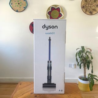 Dyson WashG1 in the box in front of colourful wall baskets