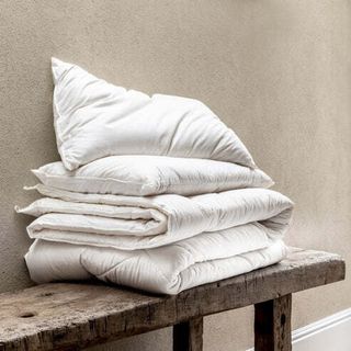 A merino woll duvet folded on a wooden bench with a pillow on top
