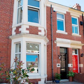 house exterior with red brick wall white window and black and red door