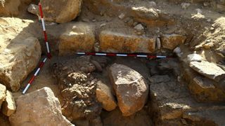 This image shows part of the excavated Sun Temple. Here we see some very large stone bricks. There are some three red and white striped poles in place to help measure the site and provide scale.