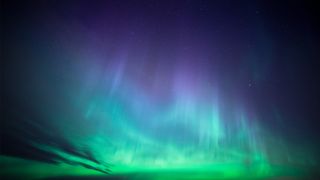 Ribbons of green, blue and purple stretch cross the sky and up towards the stars like curtains of colorful light.