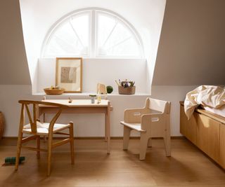 child's bedroom with wooden desk and chairs in front of a window with single wooden bed to the side