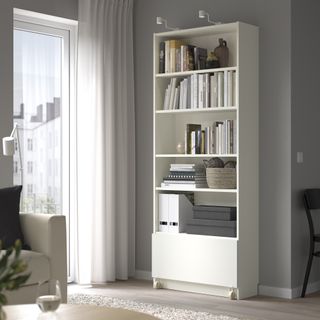 A living room with a large white BILLY bookcase with a drawer with wheels at the bottom