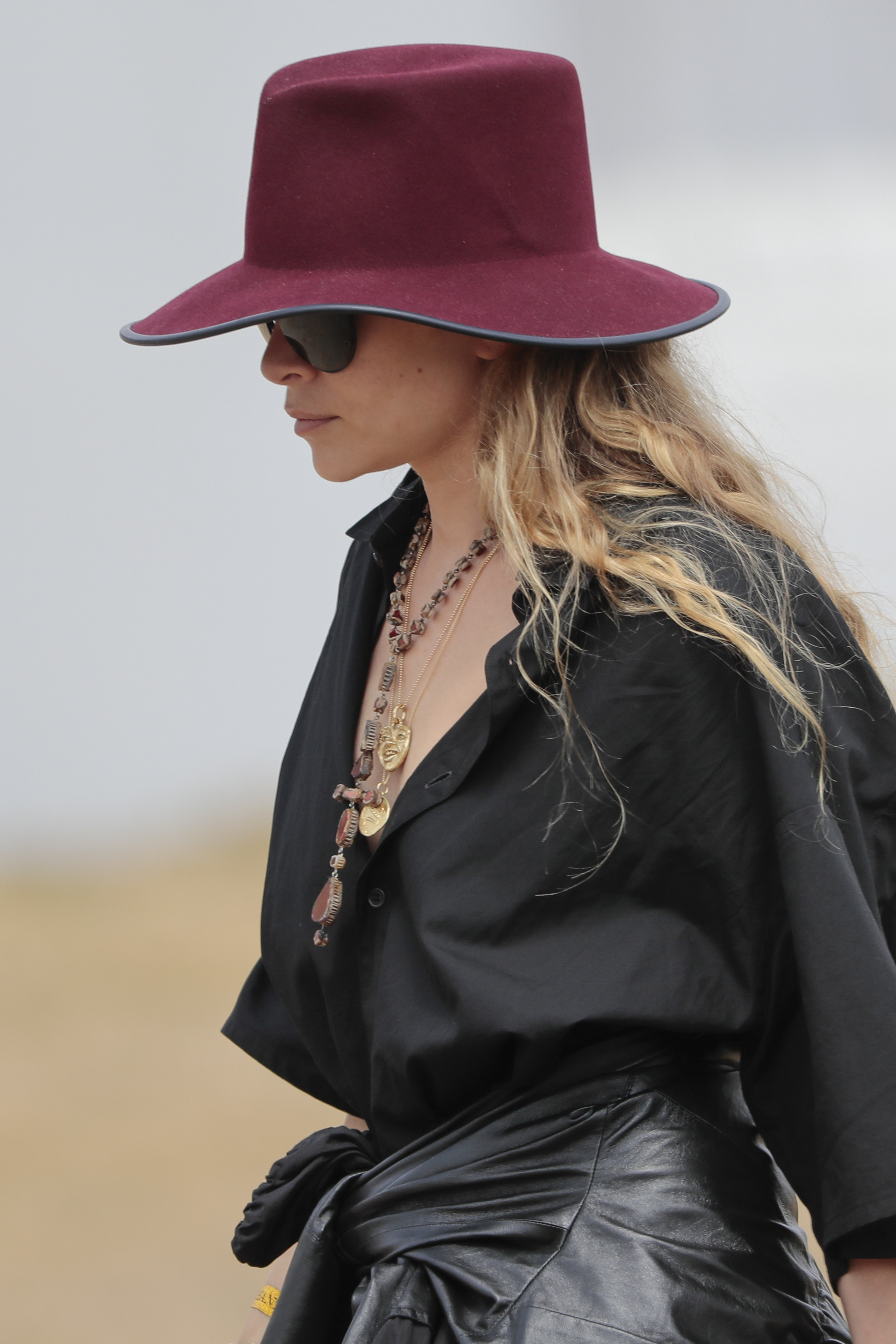 Ashley Olsen usando uma blusa preta com colares em camadas e um chapéu vermelho de abas largas.