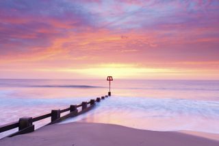 Groyne extending in sandy beach at sunset