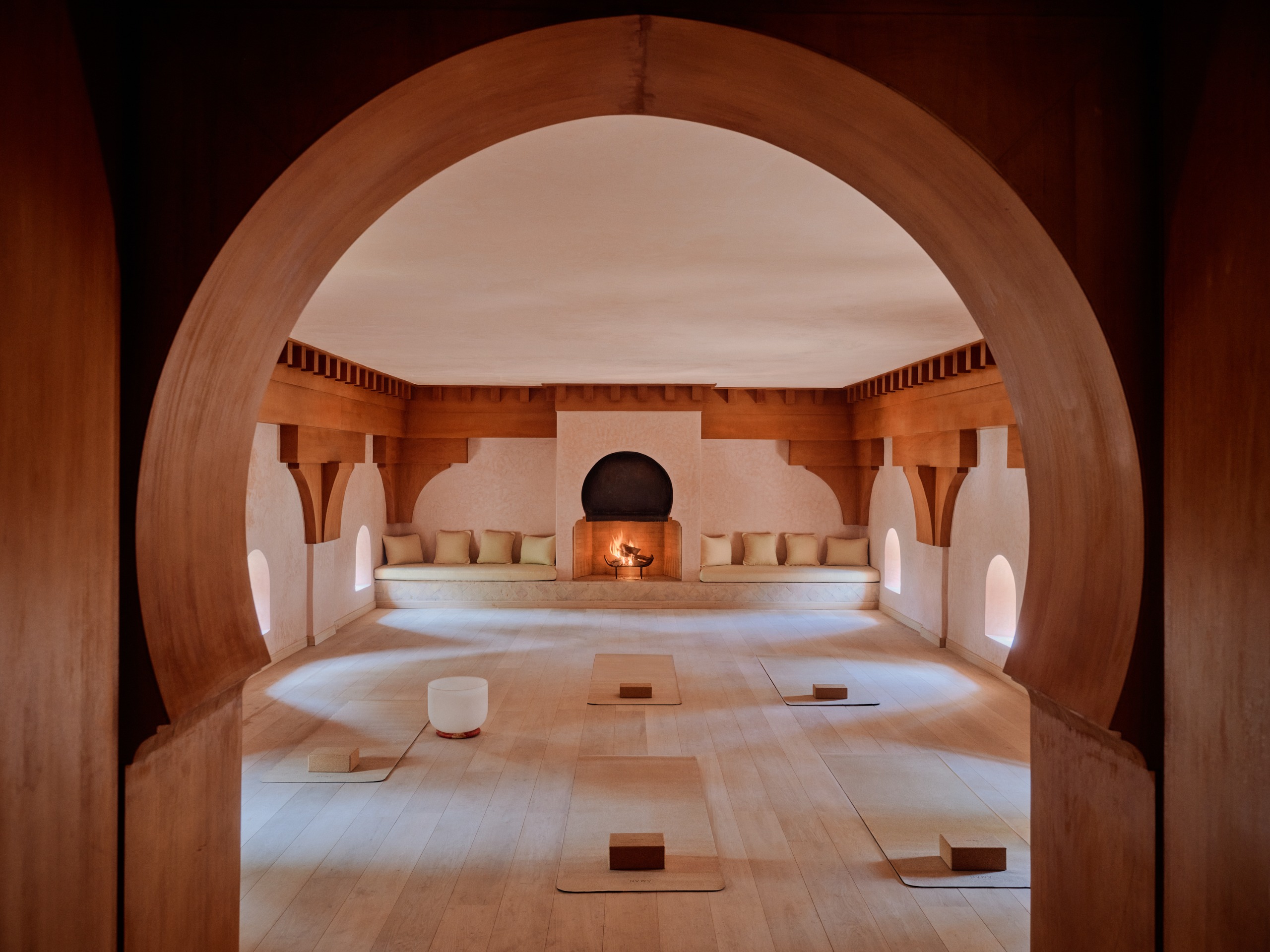 Amanjena's spa, wellness, and yoga studio, with an arched entryway, a central fireplace, and a terracotta color palette.