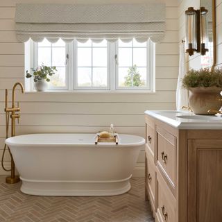 rustic bathroom with white freestanding bath with brass floor-mounted tap and wooden vanity unit