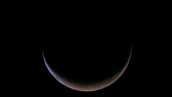 A crescent looks slightly reddish against a dark black sky.