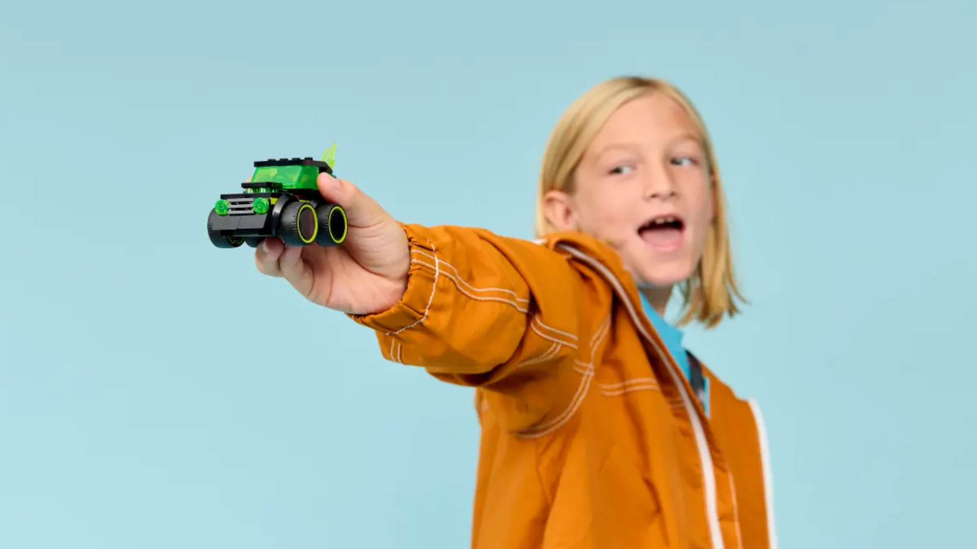 A child smiles while holding the Lego Rides - Gaming Race Car set