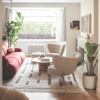 A bright living room with a curved red sofa, a round stone coffee table and two boucle accent chairs with curved backrests