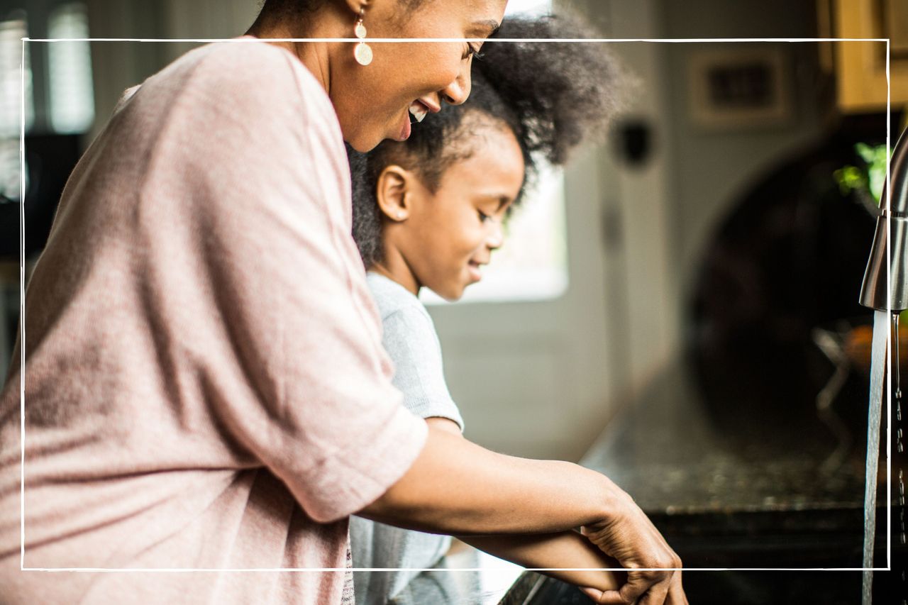 mother and daughter at home washing up together at the kitchen sink