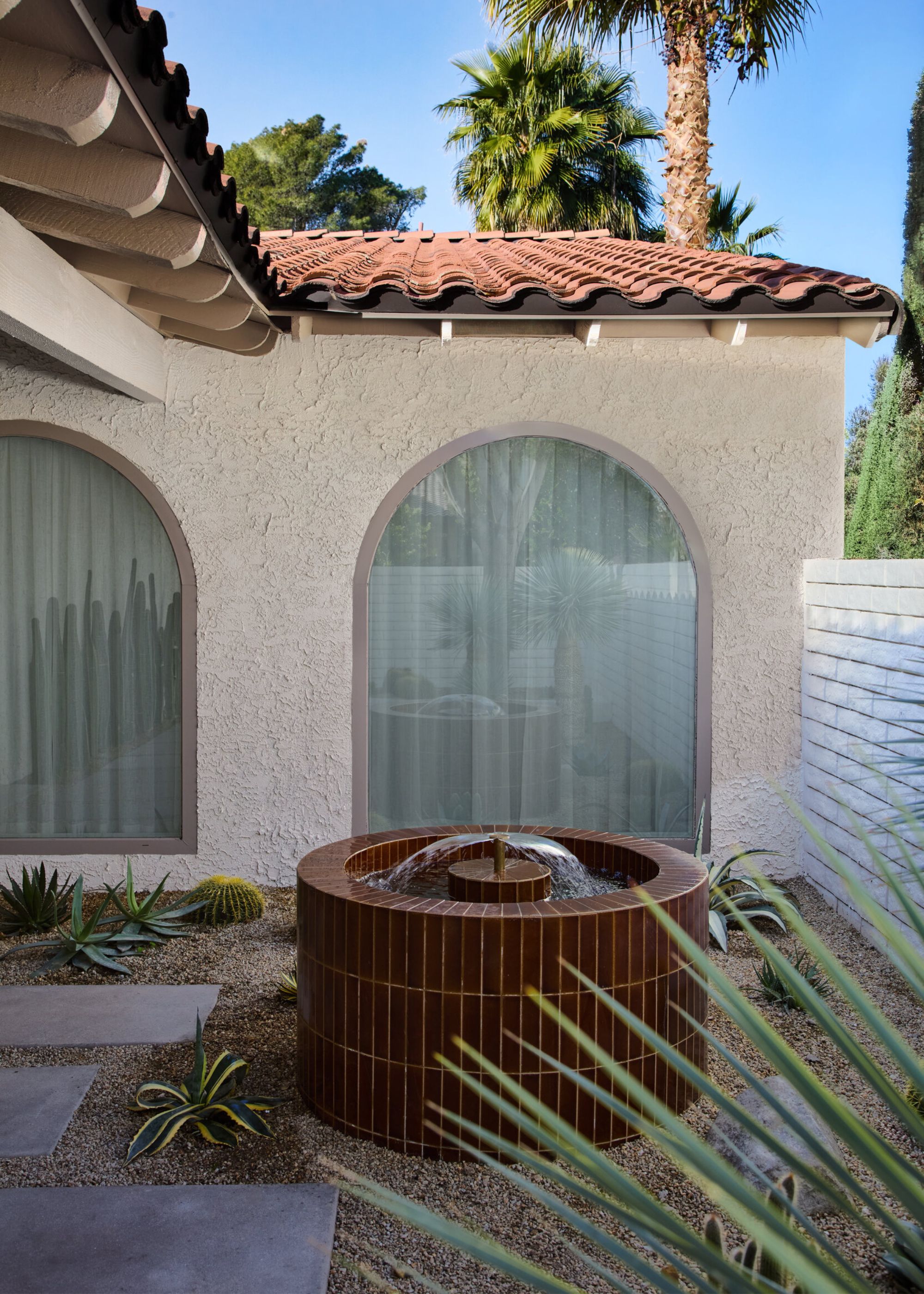 A garden with a tiled water feature, a stone path, gravel, and textured walls