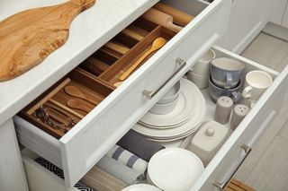 Open drawers of kitchen cabinet with different dishware, utensils and towels