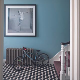 Hallway with patterned tile flooring, a bike next to stairs and art on wall.
