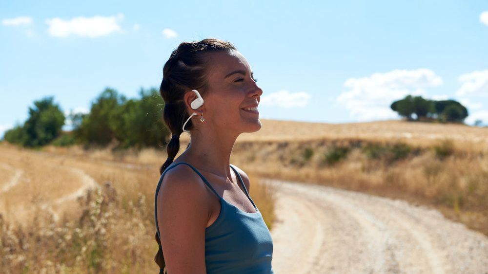 JBL Soundgear Sense earbuds worn outside by a woman next to a field