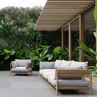 A wooden garden sofa and chair in an outdoor space filled with tropical green planting
