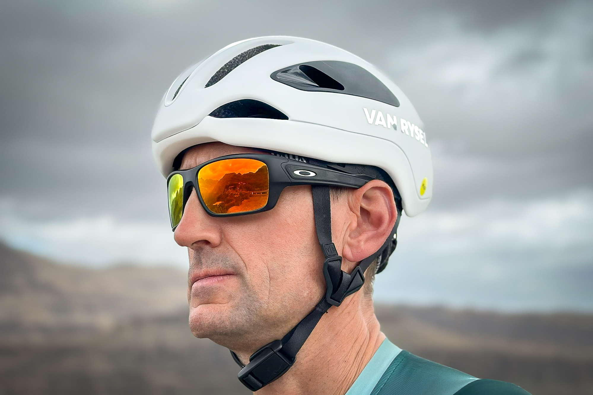 side view of a man wearing a white helmet, green jersey, black sunglasses