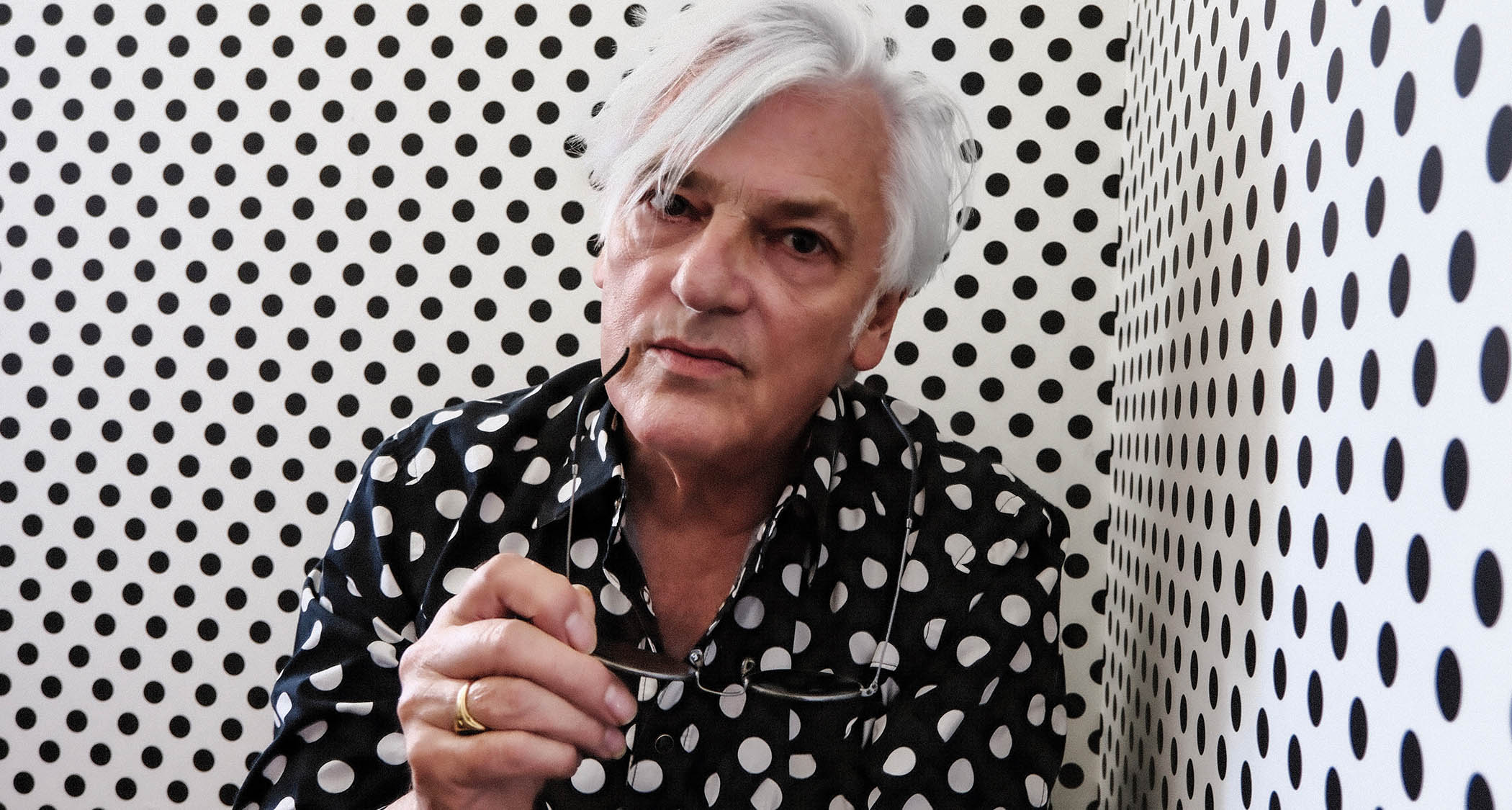 Robyn Hitchcock wears a black and white polka dot shirt and is photographed against a white and black polka dot wall.