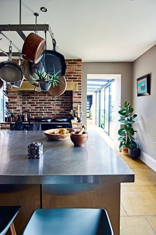 kitchen island with steel worktop pan rack above and exposed brick surround above black range cooker