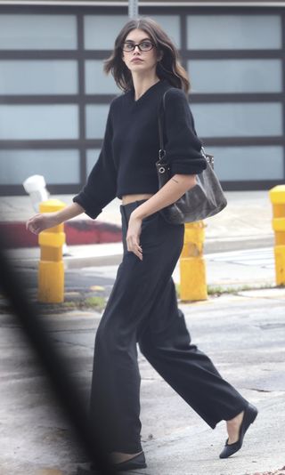 A photo of Kaia Gerber accessorizing her black sweater, trousers, and ballet flats with Paloma Wool's black Philana tote bag.
