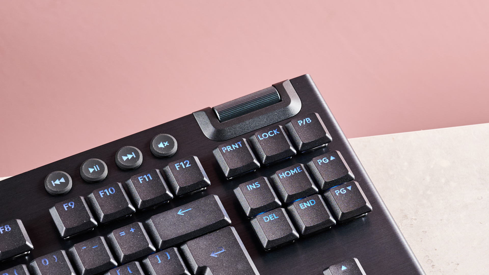 Close-up of volume wheel on Logitech G915 X, on desk with pink background