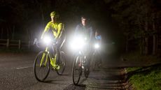 4 cyclists riding through the night, with lights at full beam. One is dressed in dark clothes and one in full fluorescent jacket, helmet and bike. In a 2 x 2 format. 