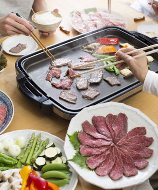 An Asian family eating a Japanese meal of grilled meats on electric Yakiniku grill with chopsticks