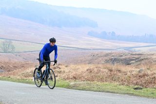 Rider in a blue jersey riding along a moorland lane on a misty day