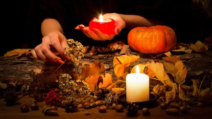 Samhain 2022: Forest witch at work on the altar. Female hands with sharp red nails among candles, herbs, pumpkin, nuts, dry leaves, acorns, ashberry, selected focus, low key