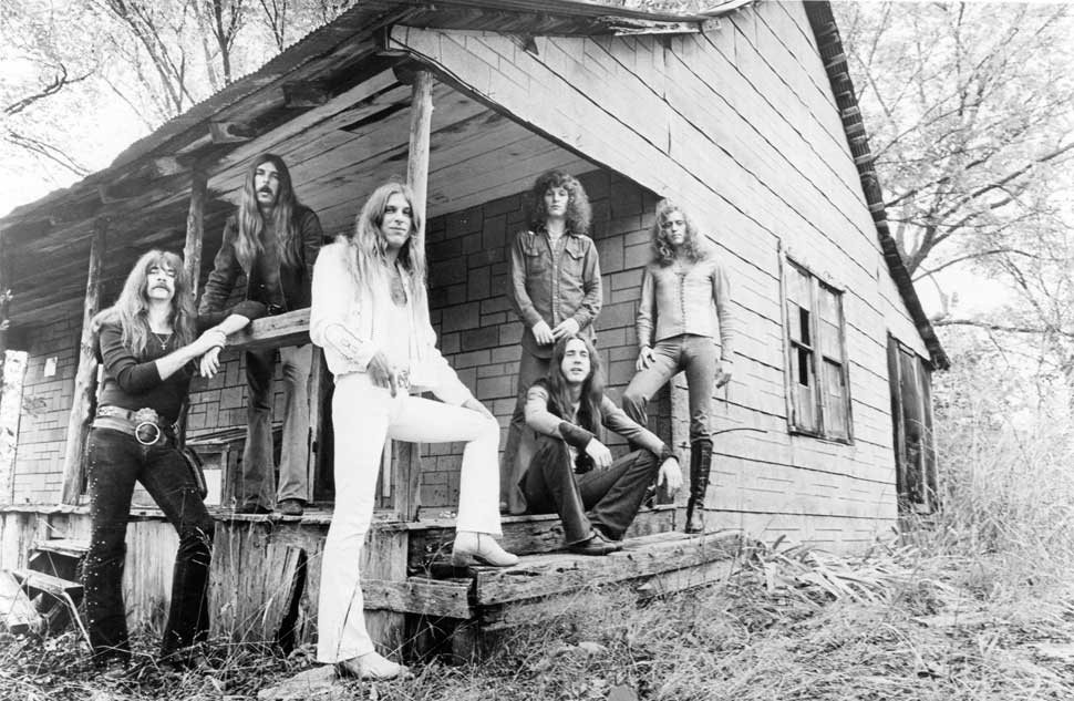 Black Oak Arkansas standing in front of a wooden cottage