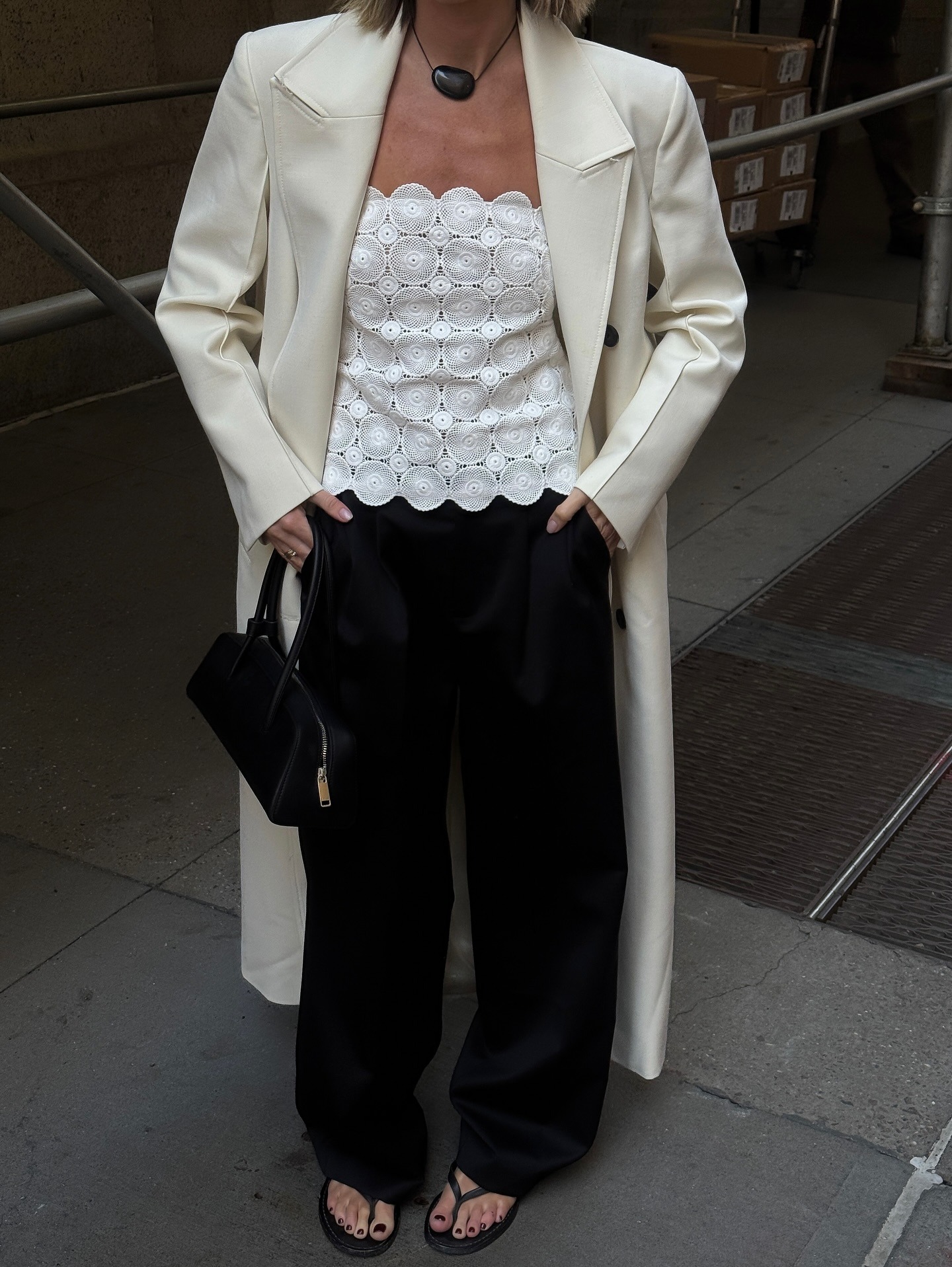 @hannahlewisstylist wearing a cream coat, white eyelet top, and black trousers.