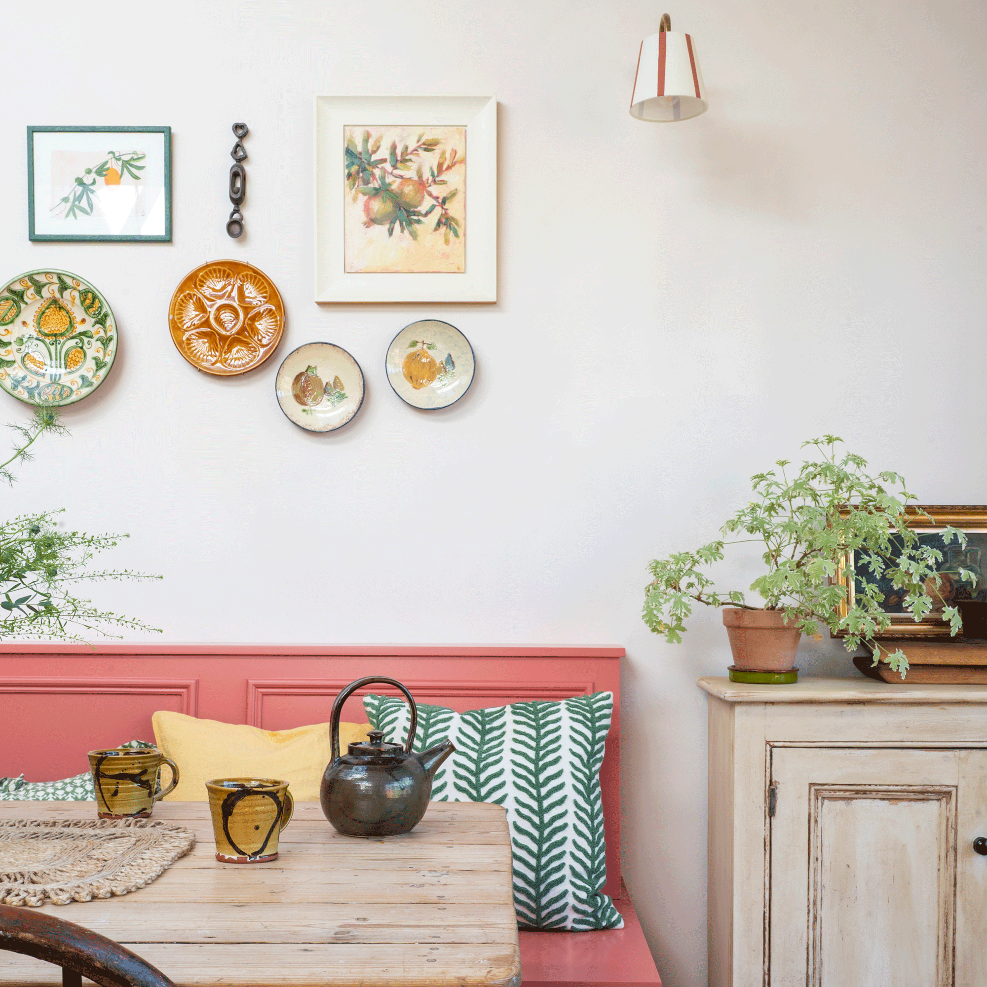 a kitchen with pink banquette seating, a plate wall above and mixed patterned cushions on the bench
