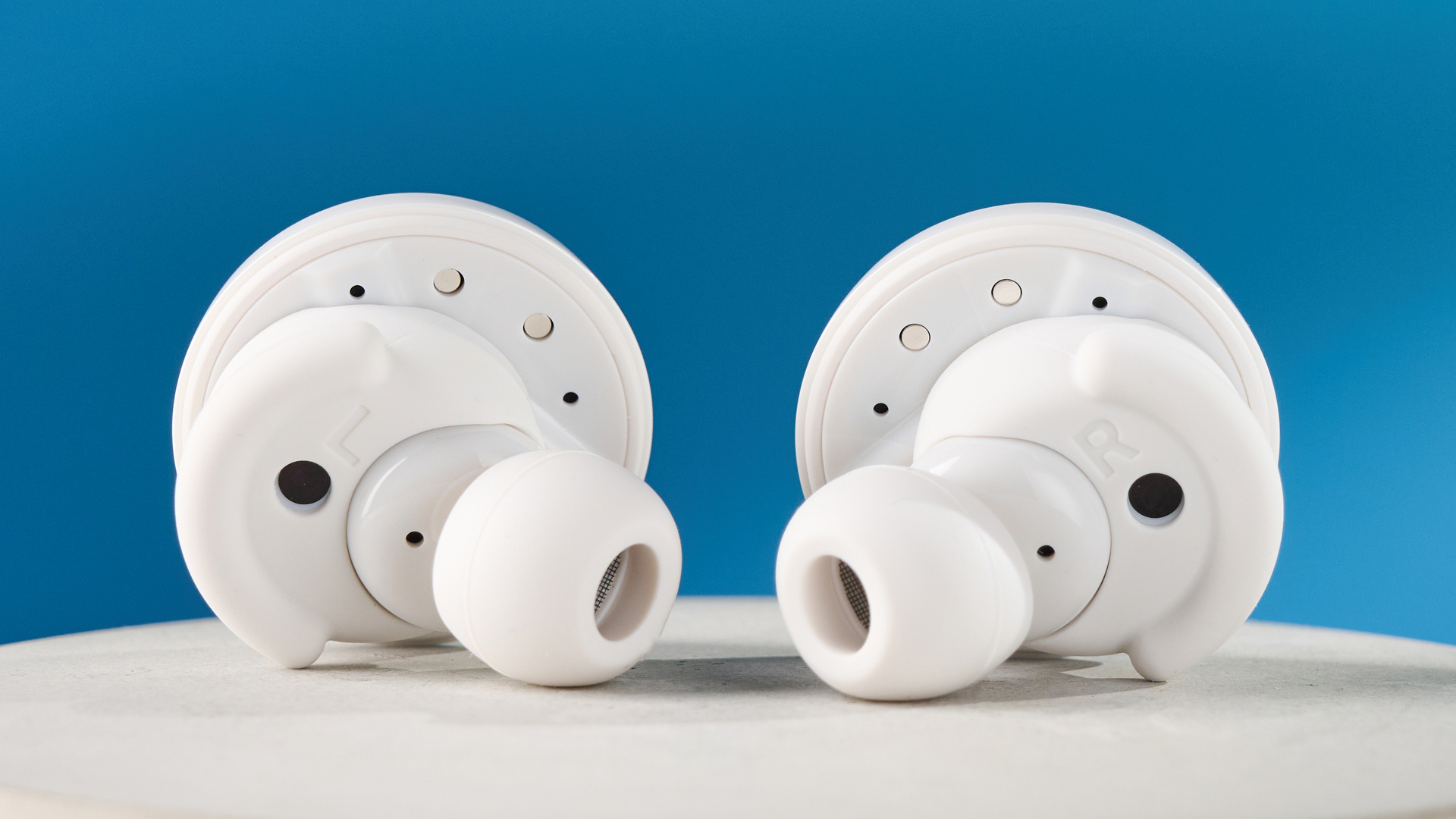 the denon perL Pro wireless earbuds in white, with circular earbud shapes, and a white charging case, photographed against a blue background